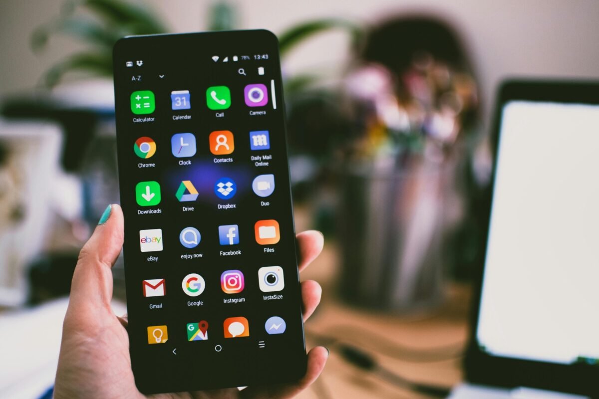 A hand holding a smartphone displaying various app icons on the home screen