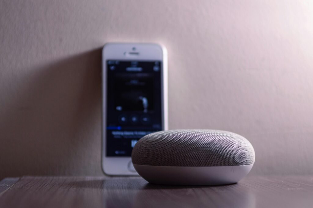 Smart speaker on a table with a smartphone in the background showing a music app interface.