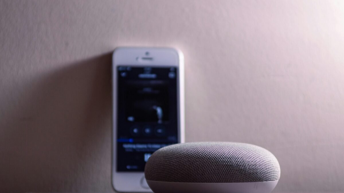 Smart speaker on a table with a smartphone in the background showing a music app interface.