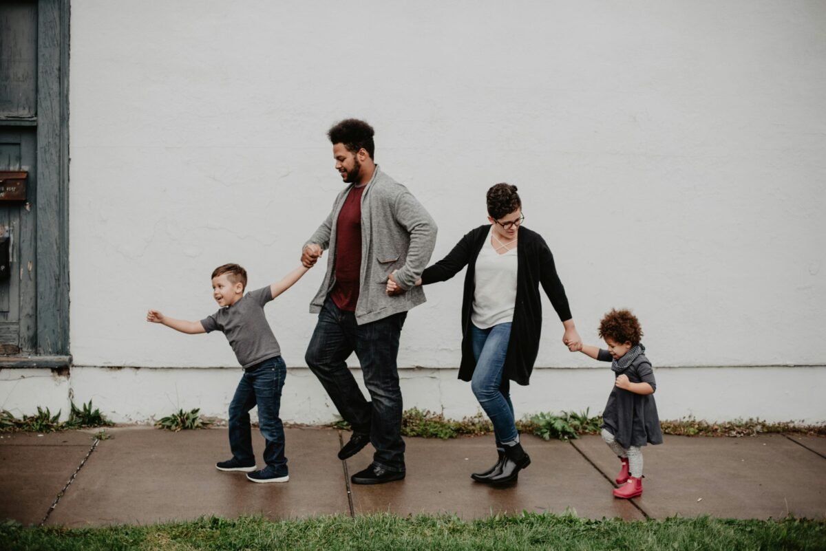 Parents walking hand-in-hand with two young children on a sidewalk, enjoying family time outdoors