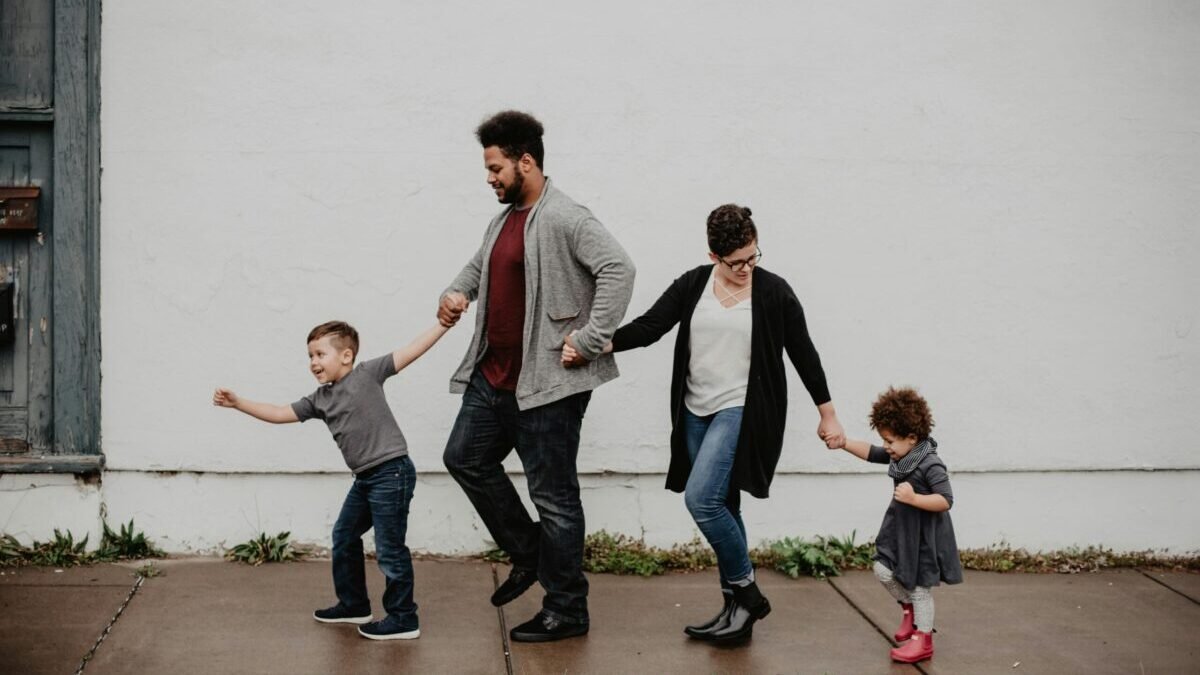 Parents walking hand-in-hand with two young children on a sidewalk, enjoying family time outdoors