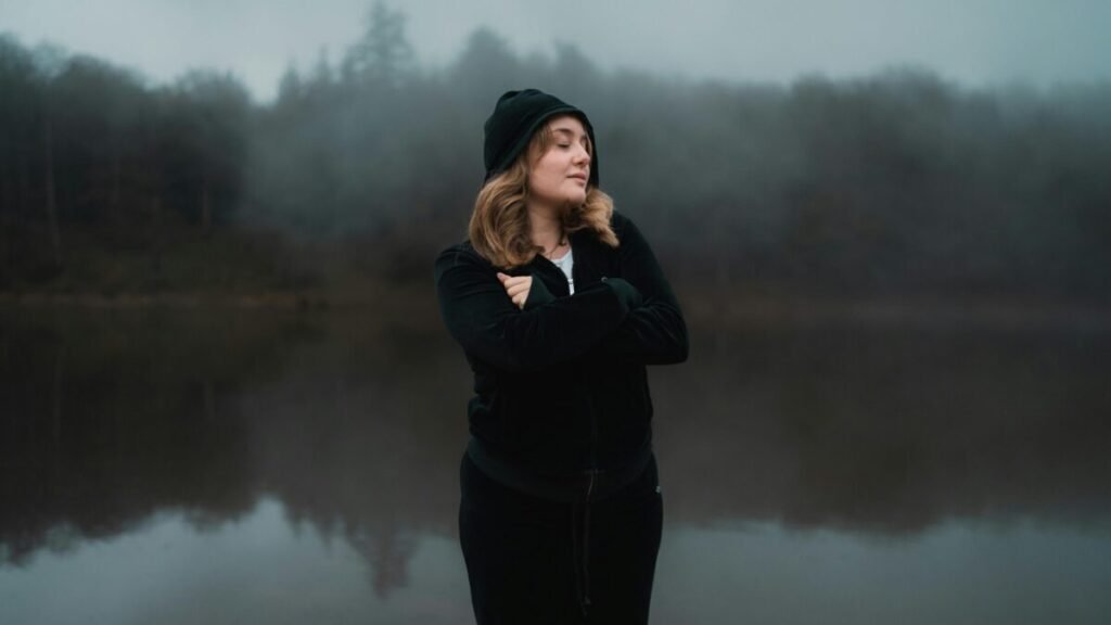 A woman standing outdoors by a calm lake during twilight, symbolizing digital balance and taking a break from screen time.