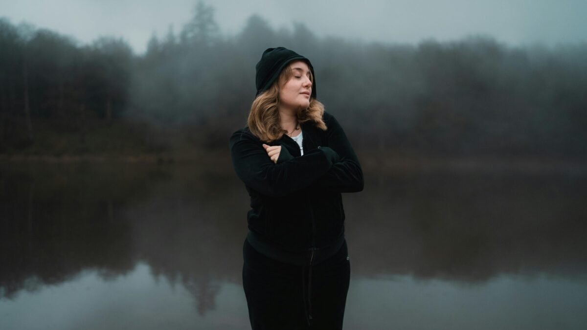 A woman standing outdoors by a calm lake during twilight, symbolizing digital balance and taking a break from screen time.