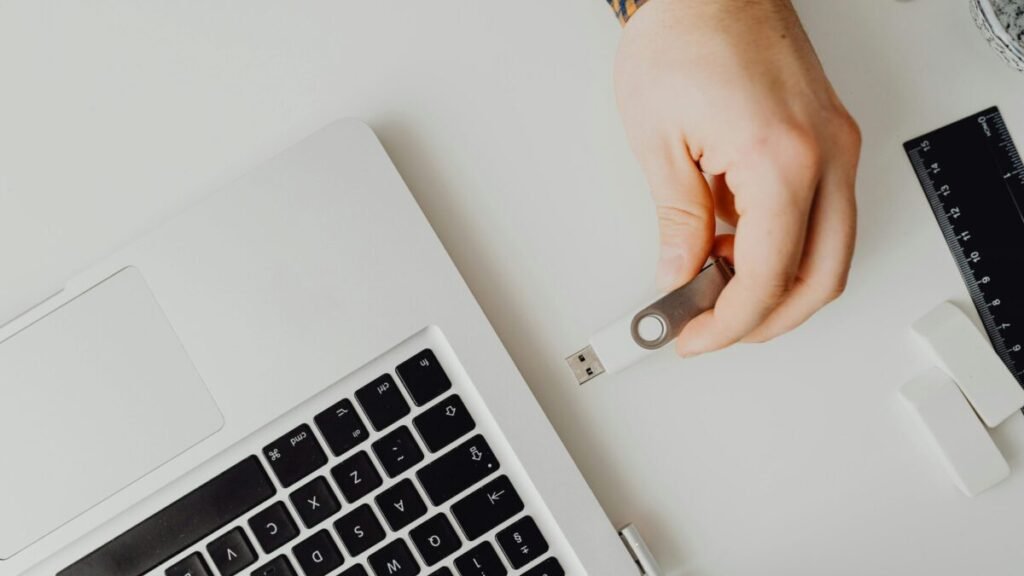 Hand inserting a USB flash drive into a laptop, representing backing up important online data.
