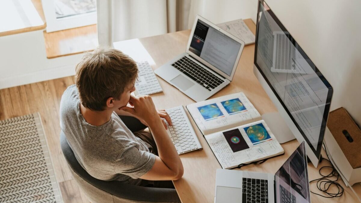 A person researching online safety on multiple laptop screens at a home desk, symbolizing protection from online scams and fake websites in 2025