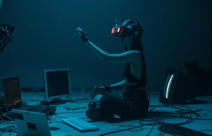 Person using advanced virtual reality headset surrounded by old and modern computer technology, symbolizing the evolution of AI and digital interaction.