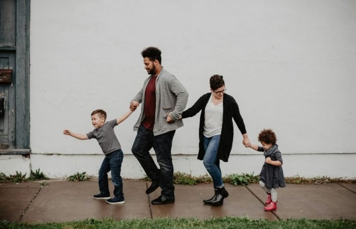 Parents walking hand-in-hand with two young children on a sidewalk, enjoying family time outdoors