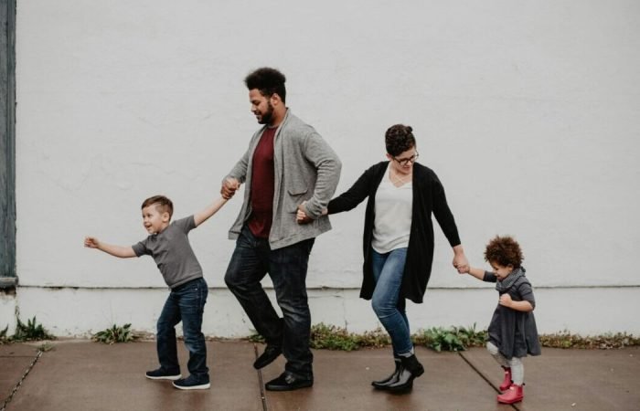 Parents walking hand-in-hand with two young children on a sidewalk, enjoying family time outdoors
