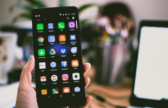 A hand holding a smartphone displaying various app icons on the home screen